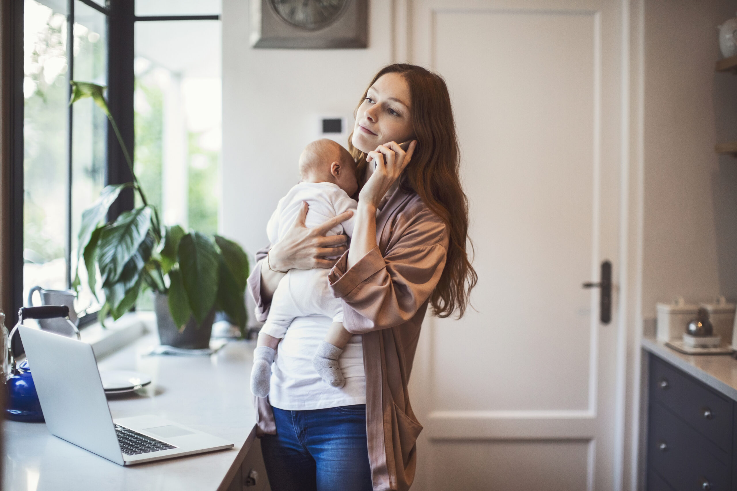 Mother using phone while carrying baby in kitchen