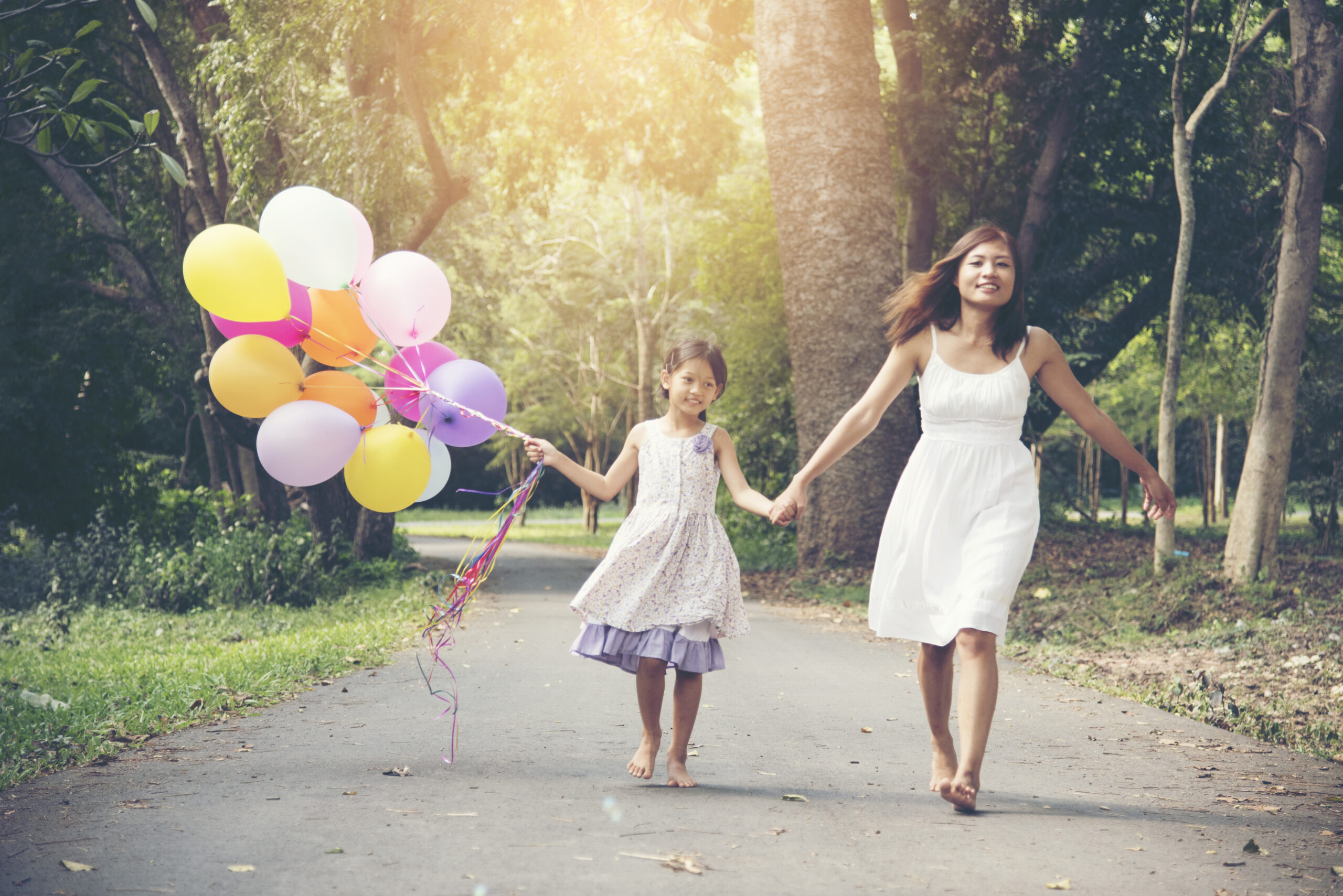 I love mom stay together on mother 's day.Adorable cute girl holding balloons with mother walking on the road in the park. Family Concept.