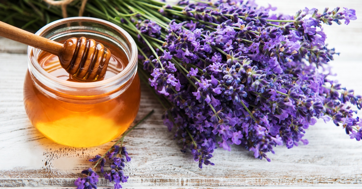 Jar with honey and fresh lavender flowers on a white wooden table