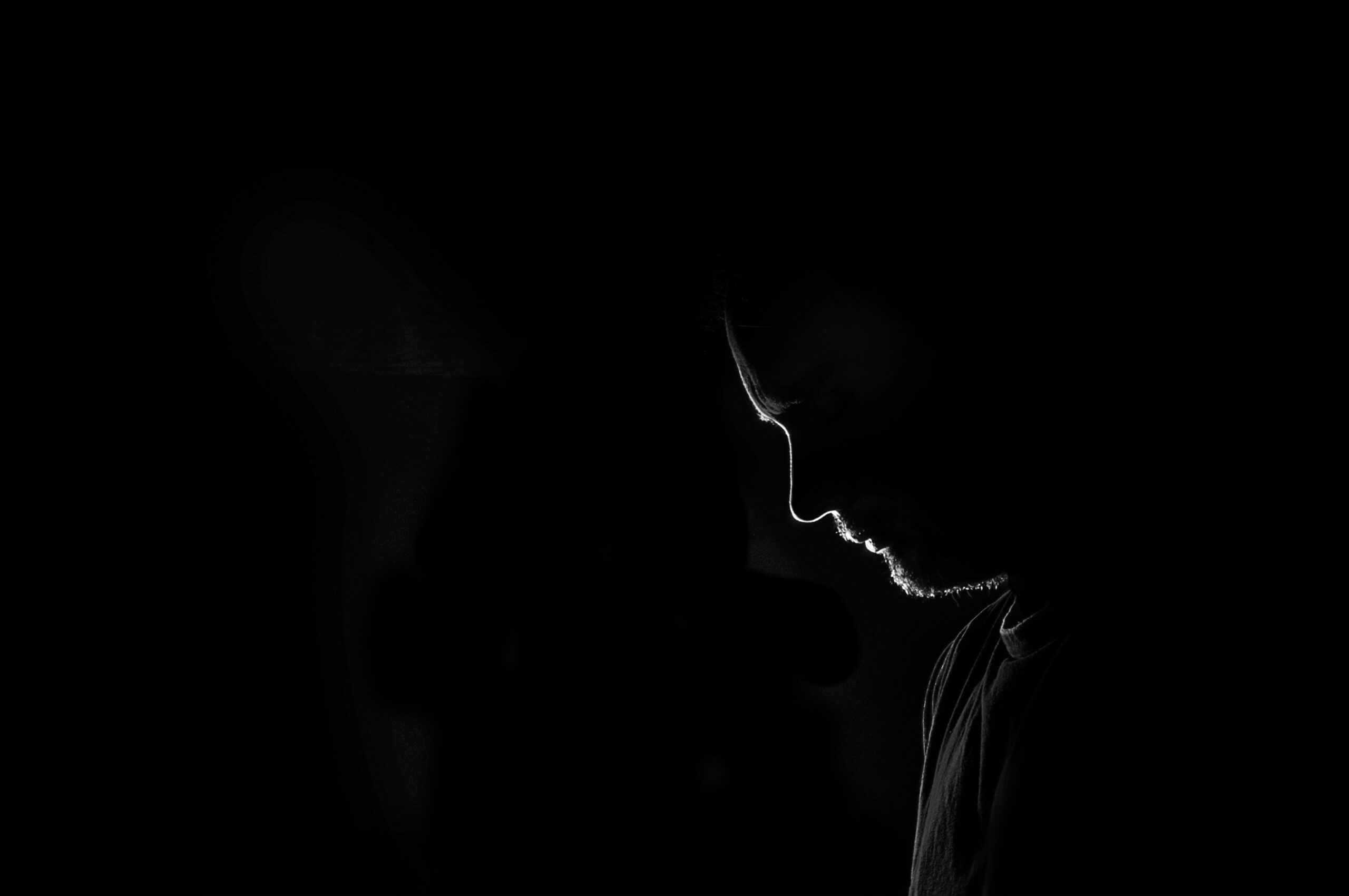 Male profile silhouette. sad or loneliness young man on black background. Unrecognizable person looking down. Image with copy space.