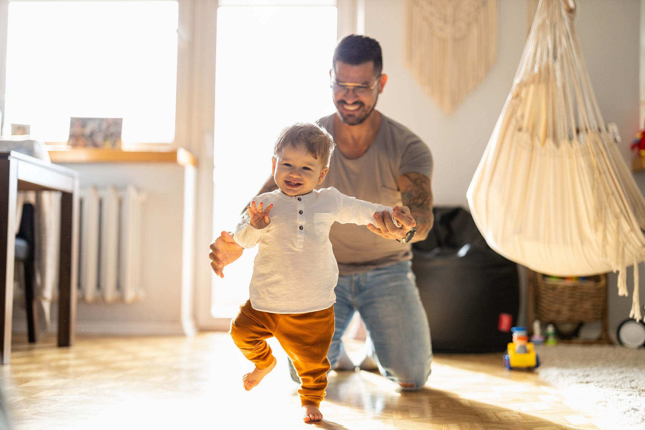 Happy father helping little son walking in living room