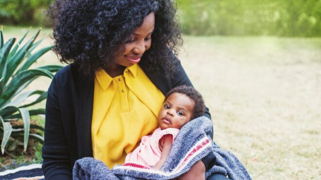 African woman holding her baby wrapped in blanket in the park