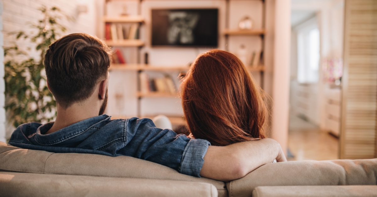 Back view of relaxed couple watching a movie on TV in the living room.