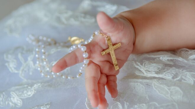 Child's hand with a crucifix on a white cloth.