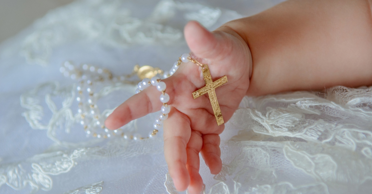 Child's hand with a crucifix on a white cloth.