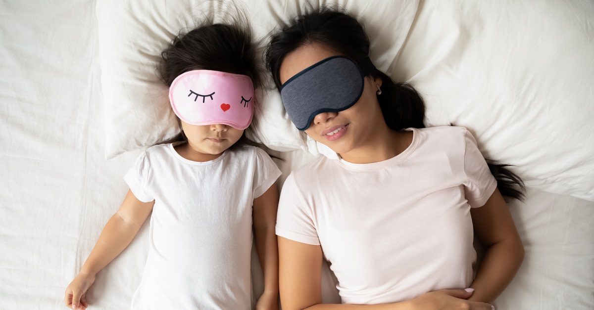 Calm Vietnamese mother and small daughter daydream in bed