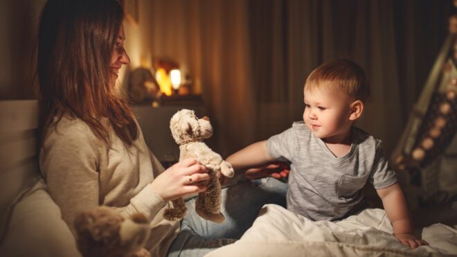 mother puts the baby son to sleep in evening in bed in dark