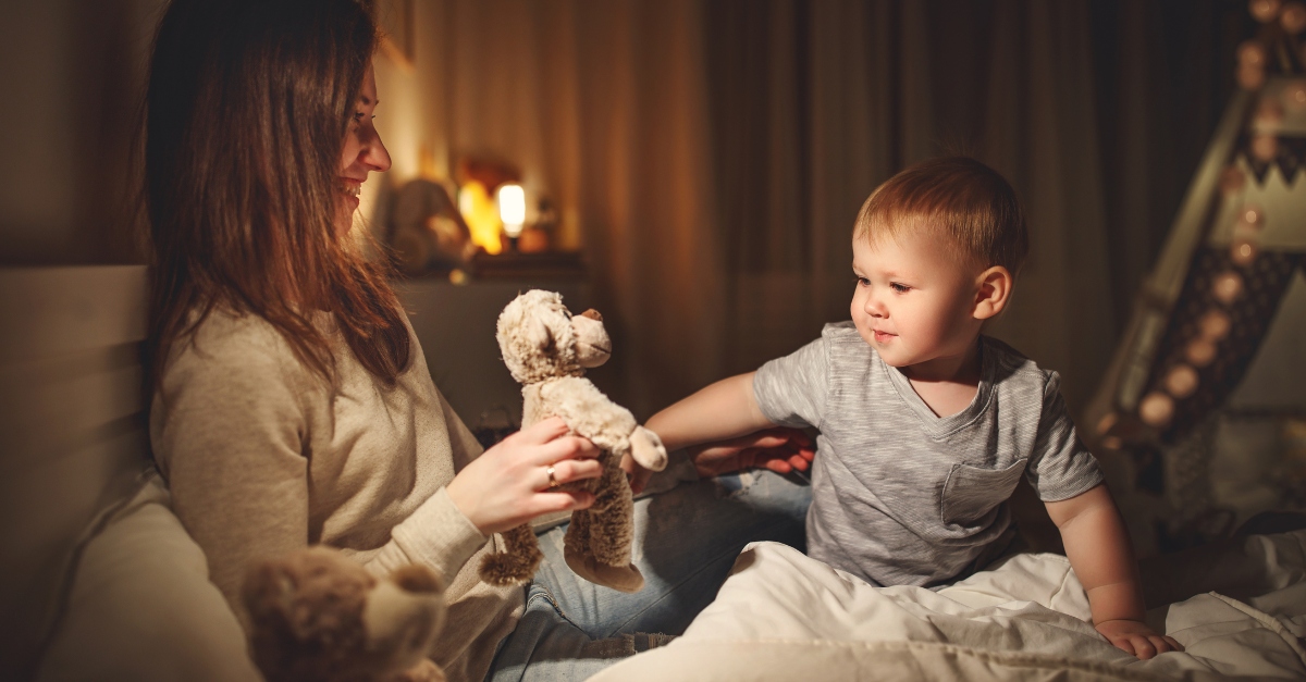 mother puts the baby son to sleep in evening in bed in dark