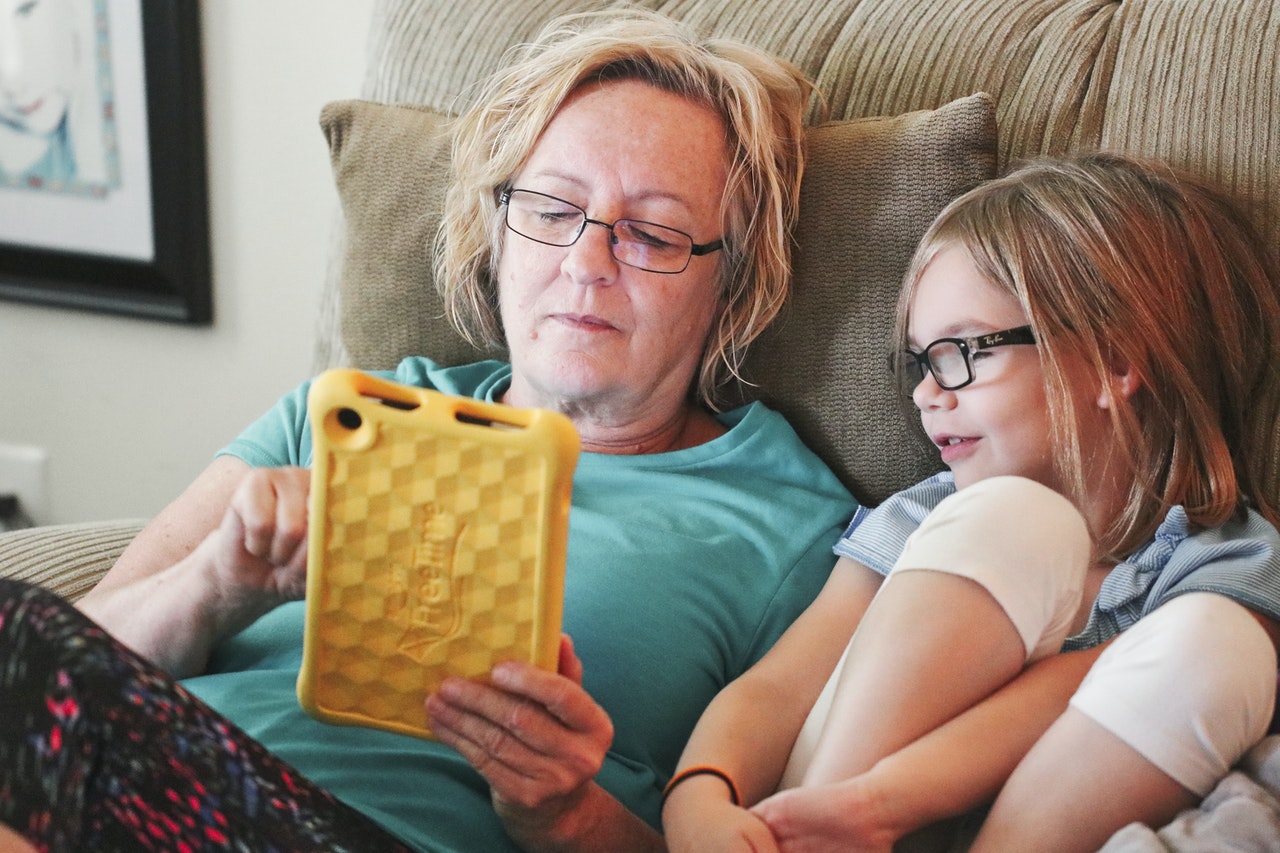 woman-holding-tablet-lying-beside-girl-wear-eyeglasses-1310121.jpg