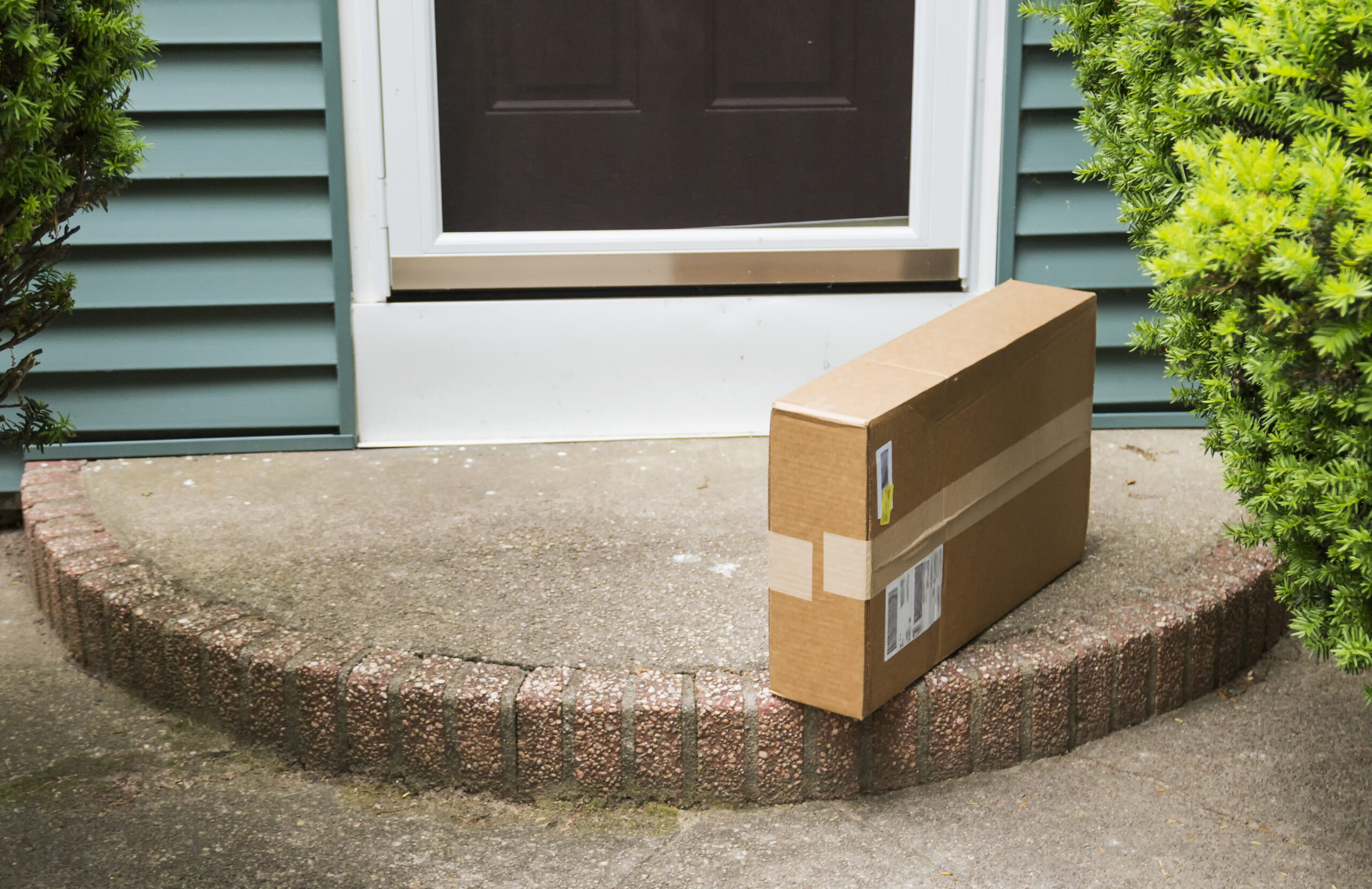 A brown cardboard box is left on the front stoop after being delivered while no one was home.