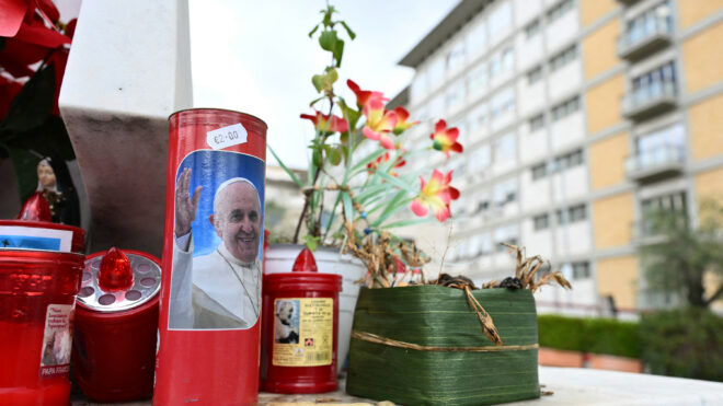 A candle with a picture of Pope Francis is set at the bottom of a statue of Pope John Paul II at the Gemelli hospital where Pope Francis is hospitalized for tests and treatment for bronchitis in Rome, on Feb. 14, 2025. The 88-year-old, who has been breathless in recent days and has delegated officials to read his speeches, was admitted following his morning audiences, the Vatican announced. (Alberto Pizzoli/AFP/Getty Images/TNS)