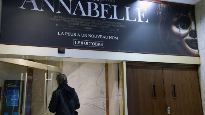 A man walks beneath a poster of the horror film ''Annabelle'' as he enters a movie theater on Oct. 22, 2014, in Paris. Paranormal investigator Dan Rivera died Sunday, July 13, 2025, in Pennsylvania on his haunted "Annabelle" doll tour. (Bertrand GuayAFP/Getty Images/TNS)