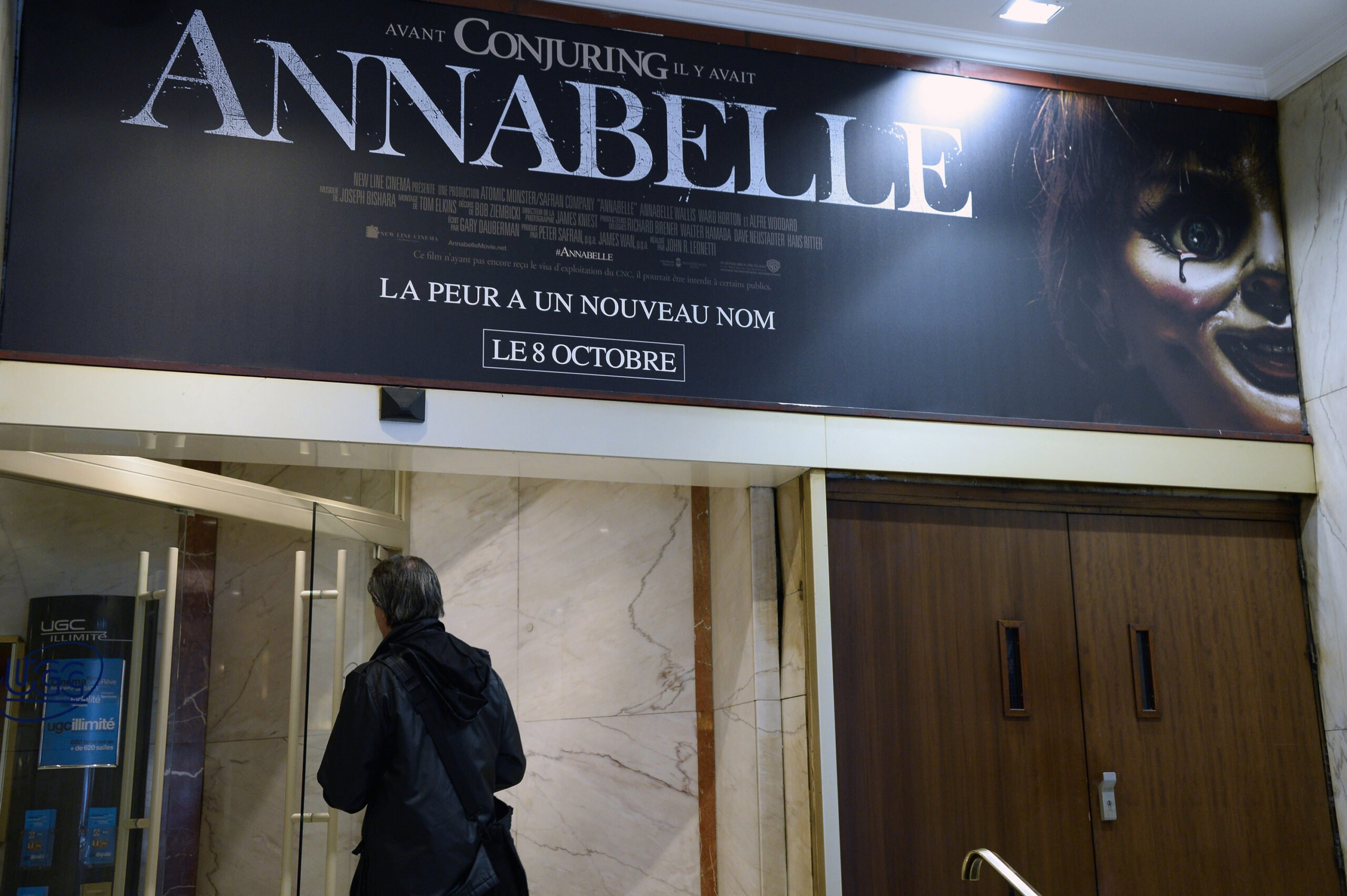 A man walks beneath a poster of the horror film ''Annabelle'' as he enters a movie theater on Oct. 22, 2014, in Paris. Paranormal investigator Dan Rivera died Sunday, July 13, 2025, in Pennsylvania on his haunted "Annabelle" doll tour. (Bertrand GuayAFP/Getty Images/TNS)
