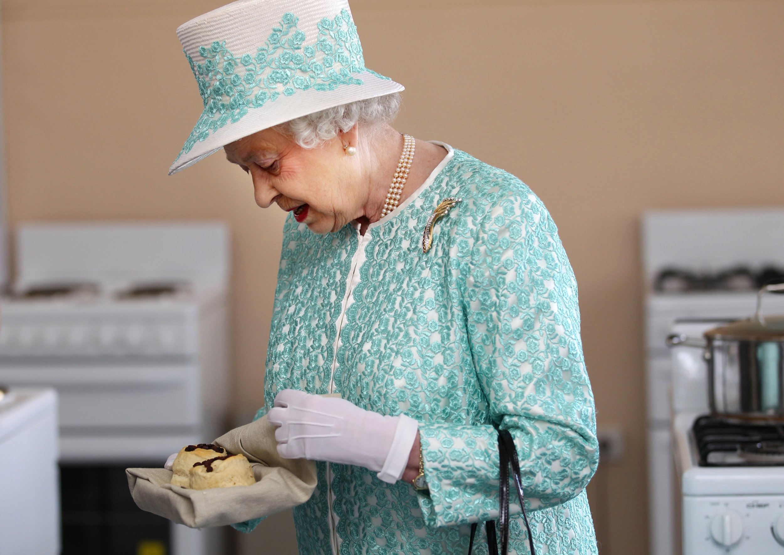 Britain's Queen Elizabeth II looks at homemade scones as she visits the kitchen at Clontarf Aboriginal College in Perth on October 27, 2011. The queen, who arrived in Perth on October 26, will officially open the 54-nation Commonwealth Heads of Government Meeting (CHOGM) on October 28 where revamping succession to the British throne will be discussed, concluding a 10-day tour of her antipodean realm. AFP PHOTO / POOL / SHARON SMITH (Photo credit should read SHARON SMITH/AFP via Getty Images)