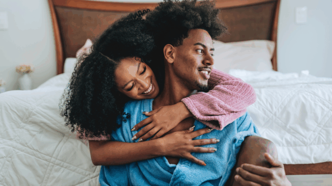 A gorgeous couple share a hug on the bed in their robes