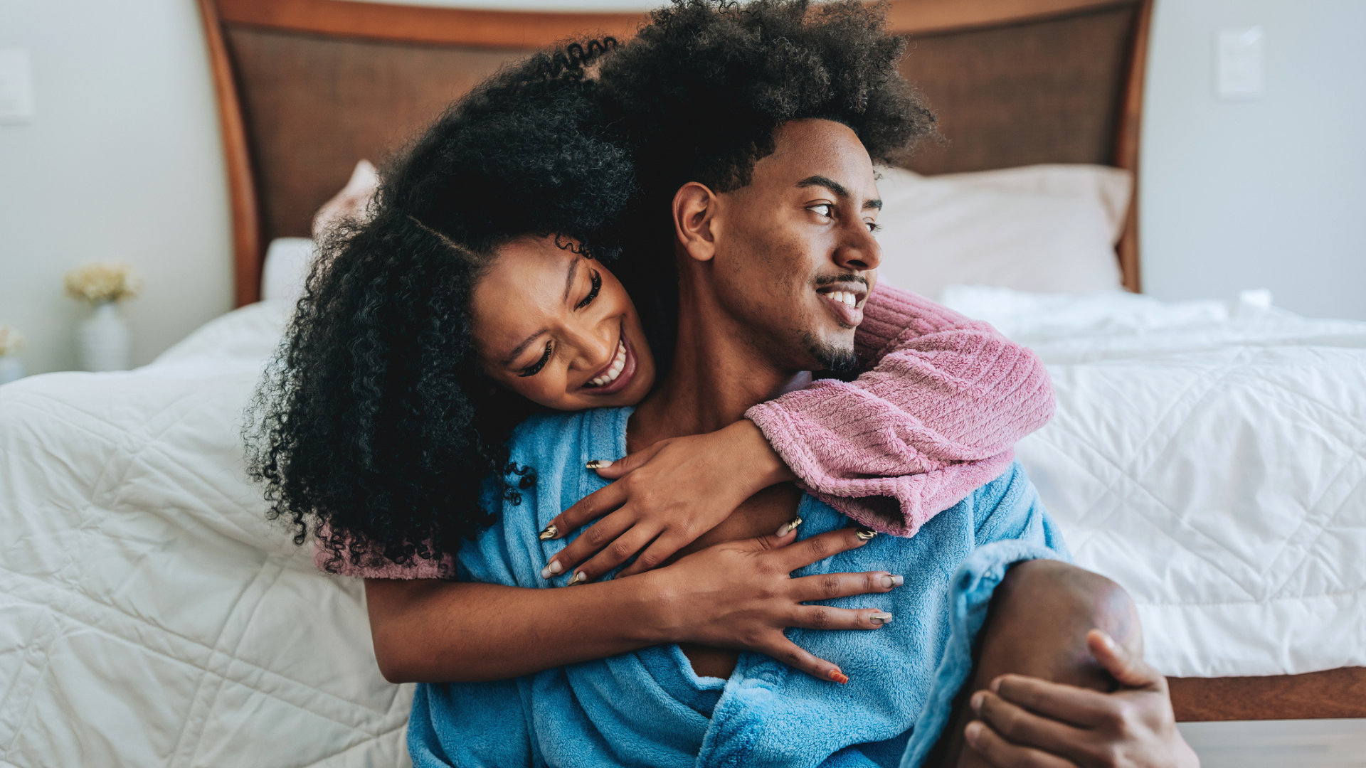 A gorgeous couple share a hug on the bed in their robes