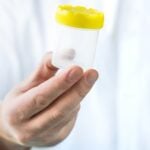 Doctor holding urine sample cup. Medical test in hospital.