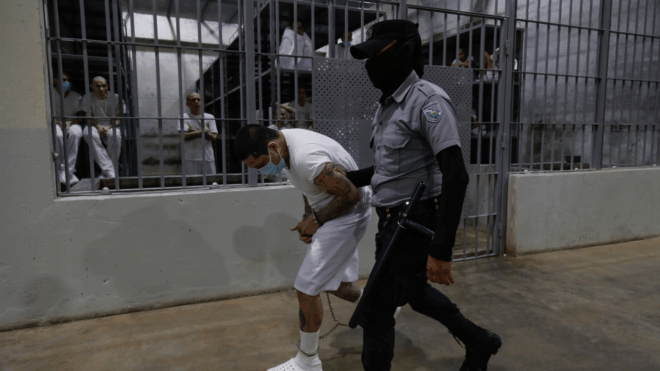 An inmate is escorted by a guard at CECOT
