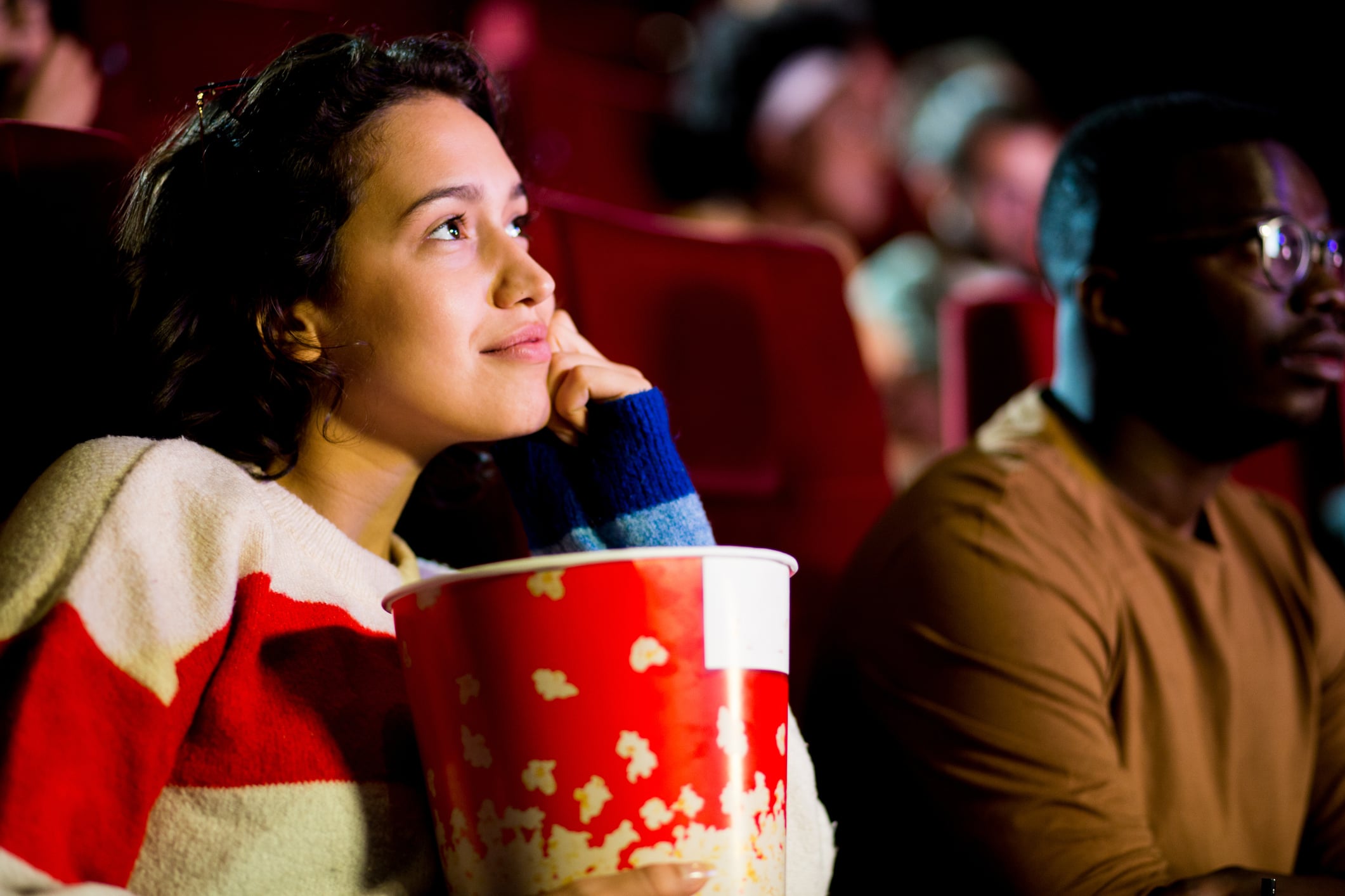 Girl watching a sad movie at the cinema with her African American friend.
