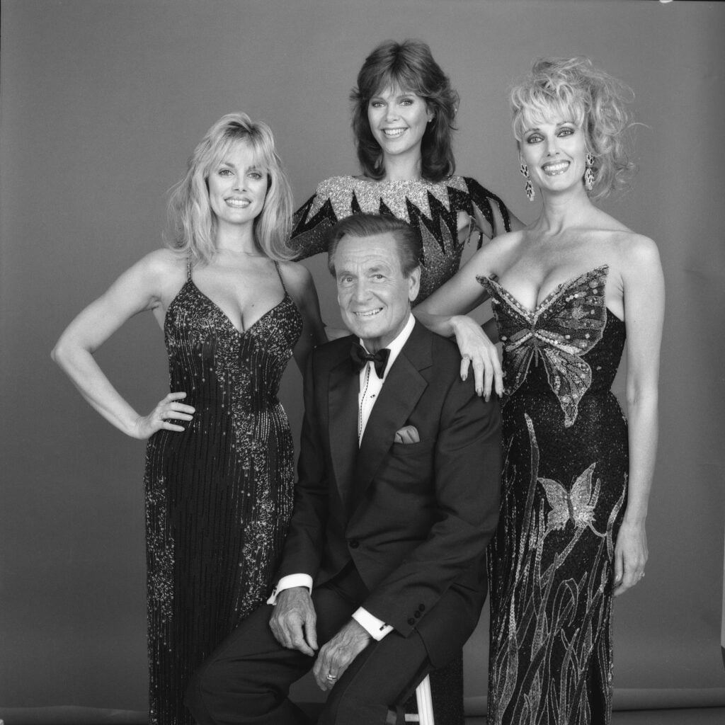 American game show host Bob Barker sits as he poses with three of the so-called 'Barker's Beauties' models, (left to right) Dian Parkinson, Holly Halstrom, and Janice Pennington, of the CBS game show 'The Price is Right,' Los Angeles, California, July 1, 1986.