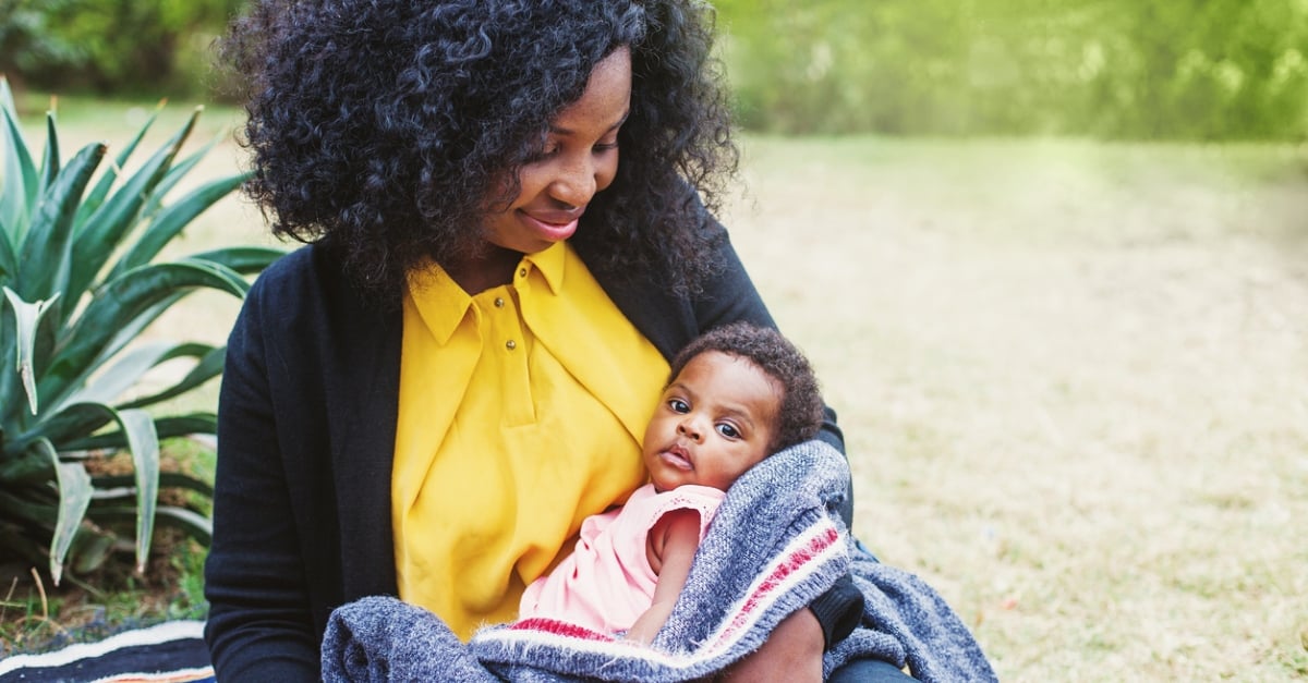 African woman holding her baby wrapped in blanket in the park