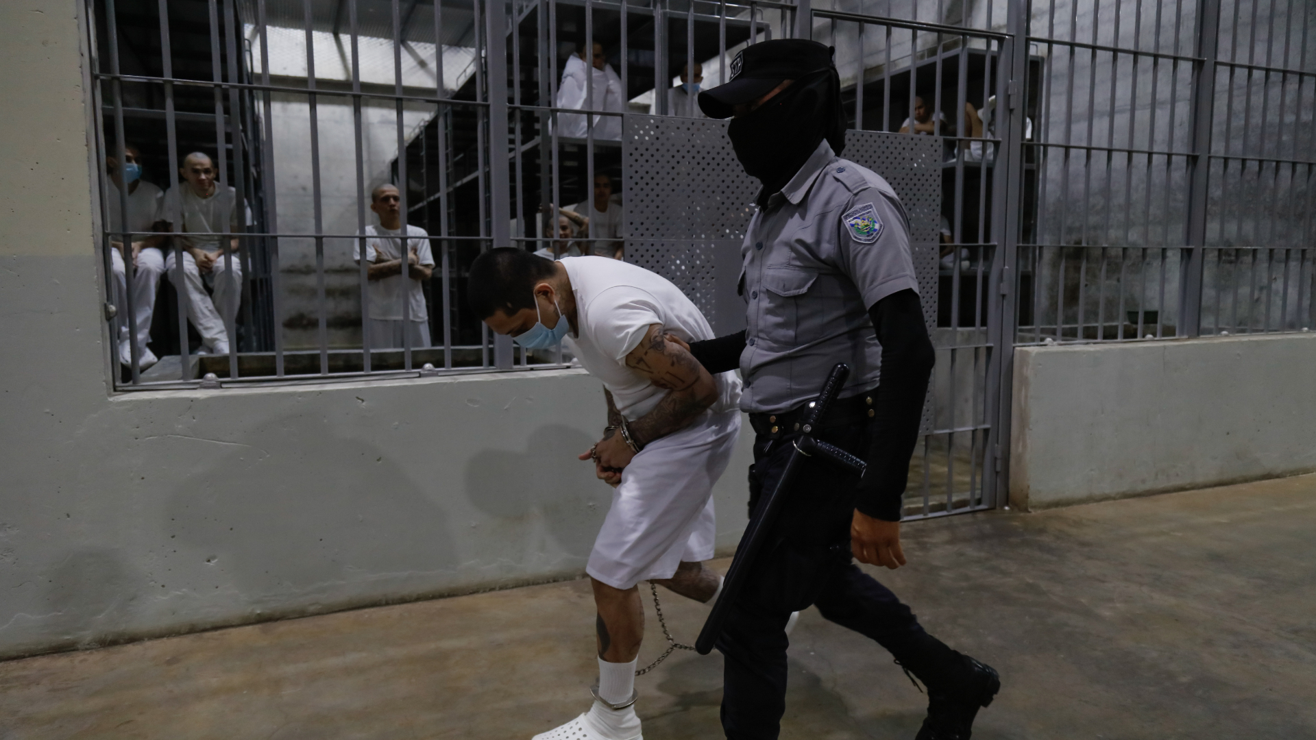 An inmate is escorted by a guard at CECOT
