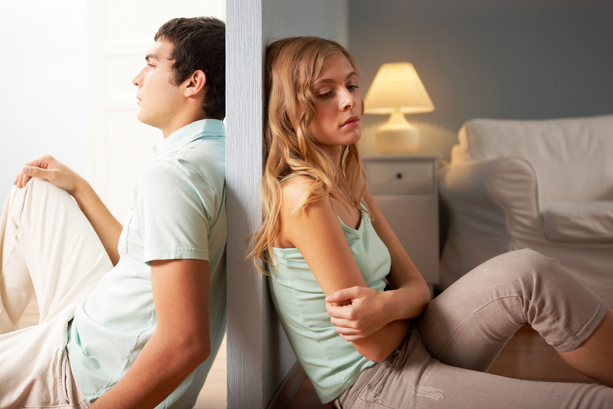 Young couple sitting on the floor on opposite sites of the wall